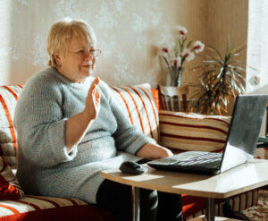 Senior mature candid real Caucasian woman look at laptop screen at home. Happy senior blonde female have online video call with family via internet. Elderly technology concept, independent retirement, senior living community